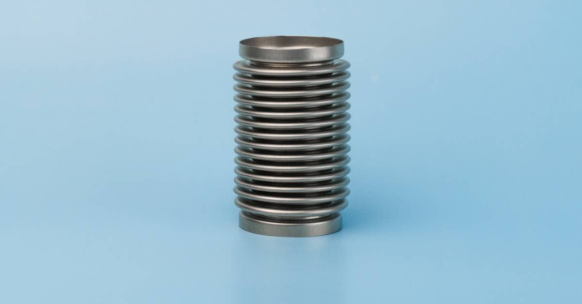 A silver metal bellows sits on a completely blue surface and in front of a background with the same color.